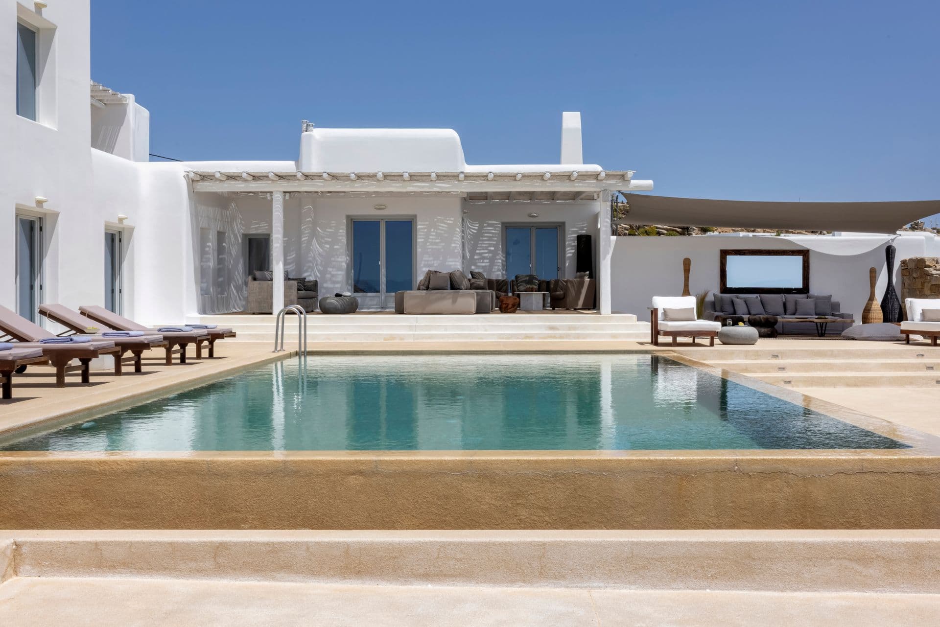 Cycladic-style whitewashed villa with sun loungers beside a large turquoise infinity pool in Mykonos