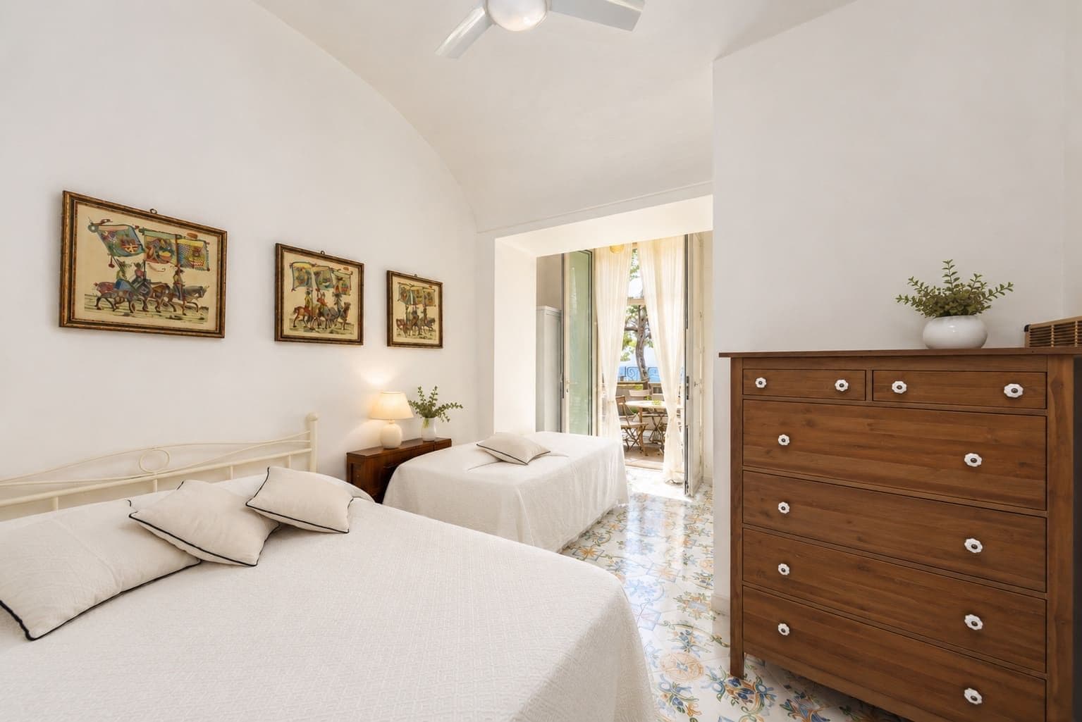 White double bedroom with an antique chest and patterned tiled floor at Faraglioni Frills, Capri