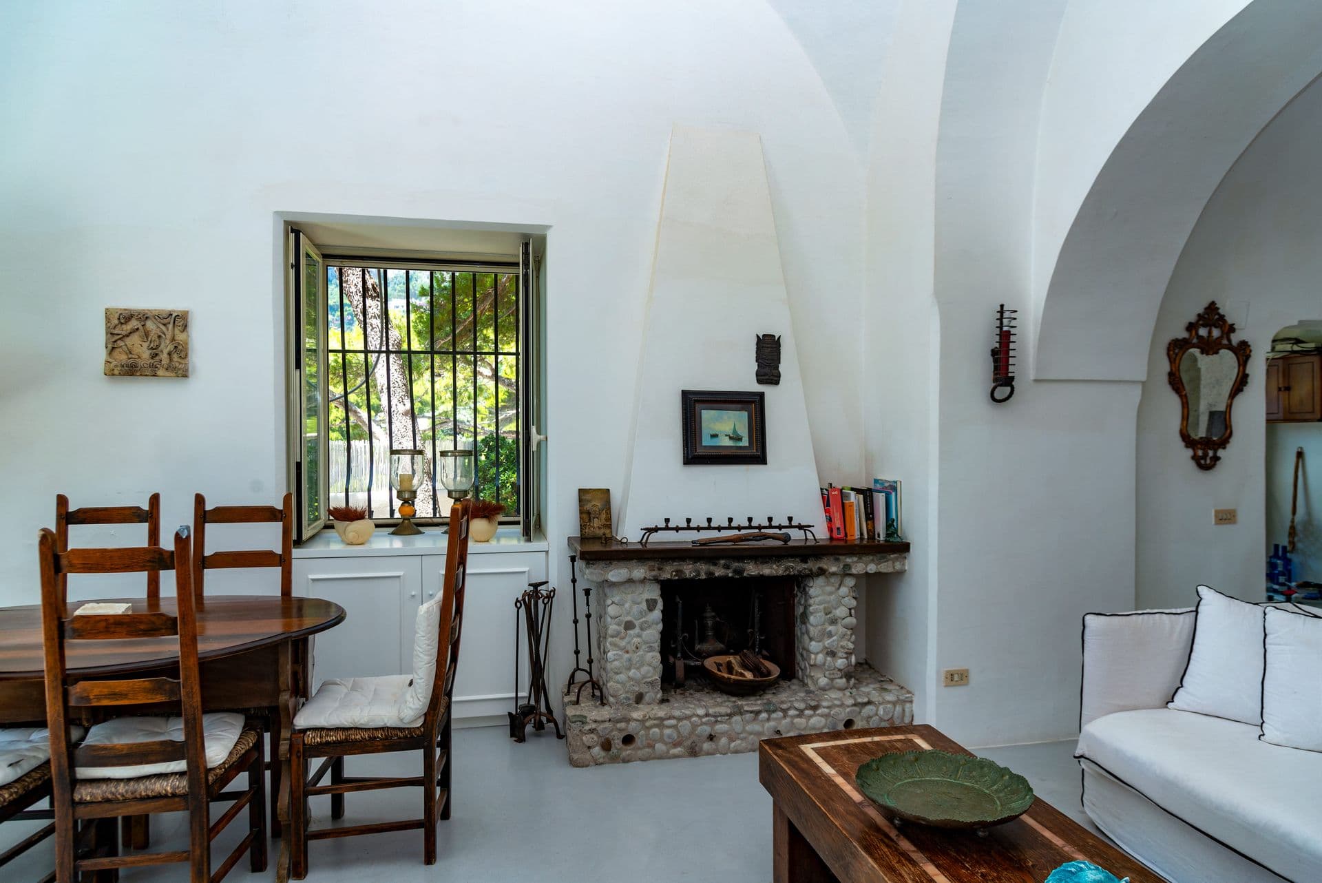 Dining table and rustic fireplace in a vaulted white room at Faraglioni Frills, Capri