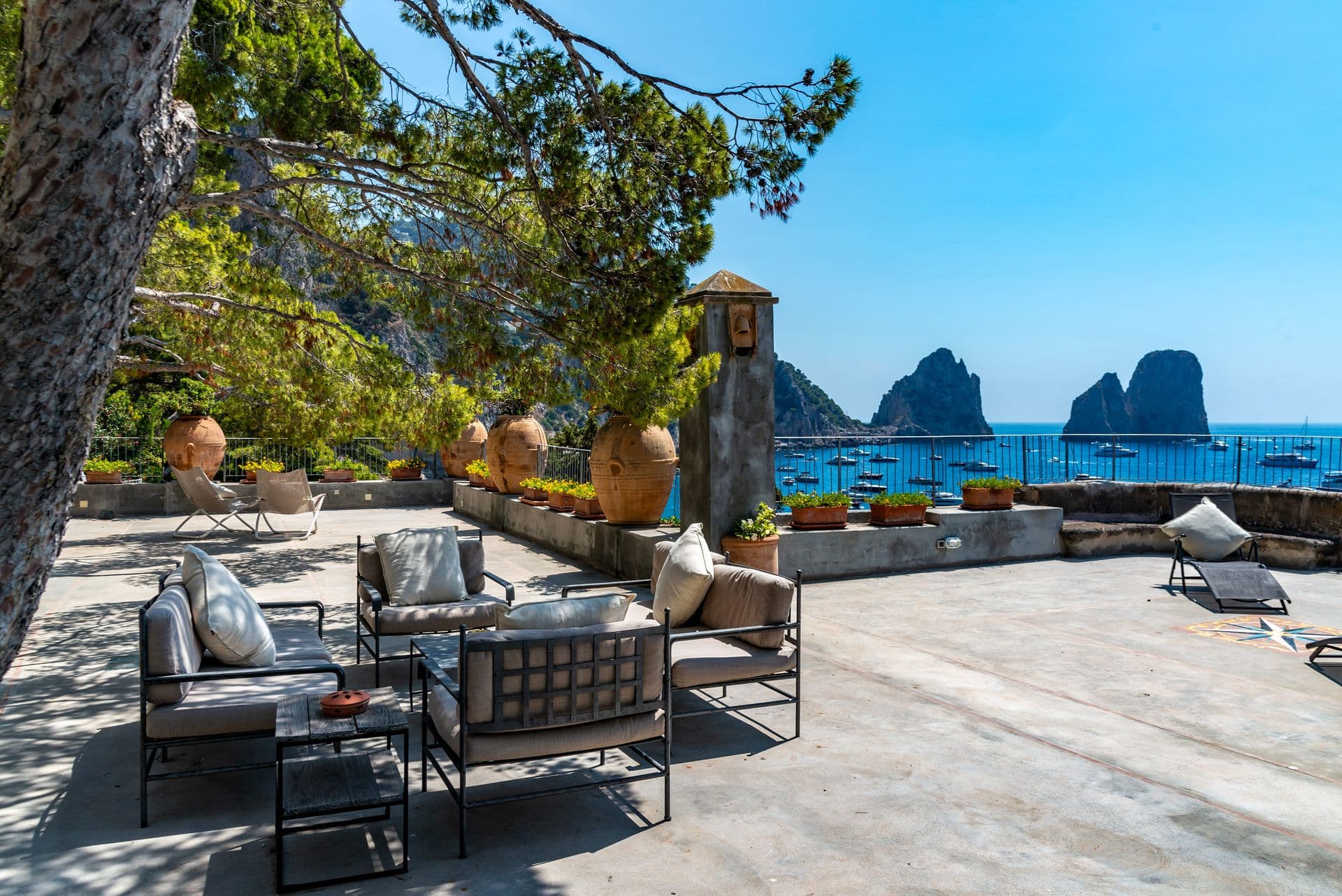 Terrace seating under pines with the Faraglioni and sea beyond at Faraglioni Frills, Capri