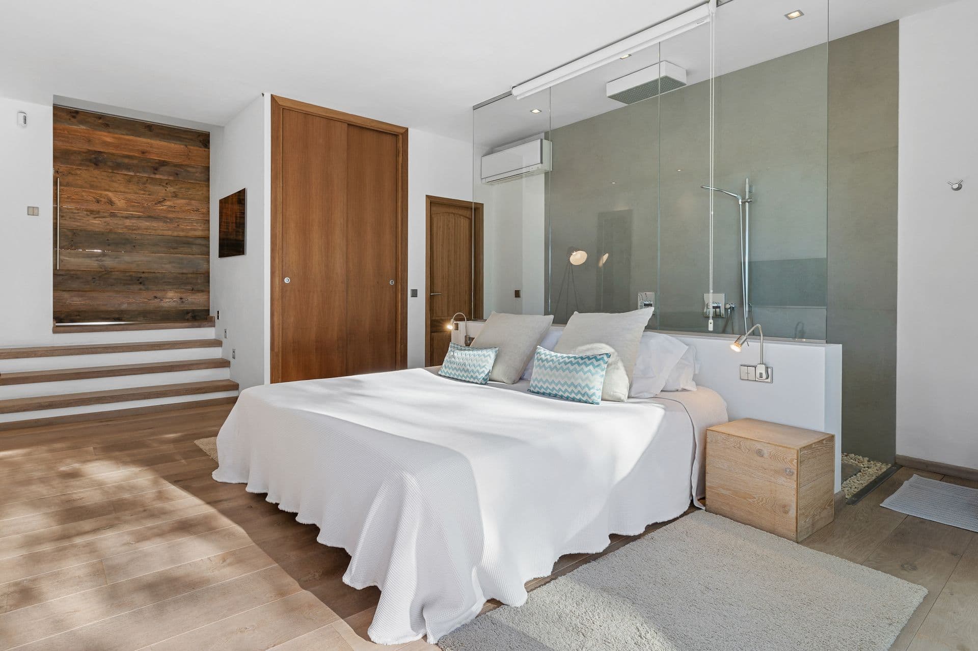 Bedroom with an open plan glass ensuite shower and wood clad steps.