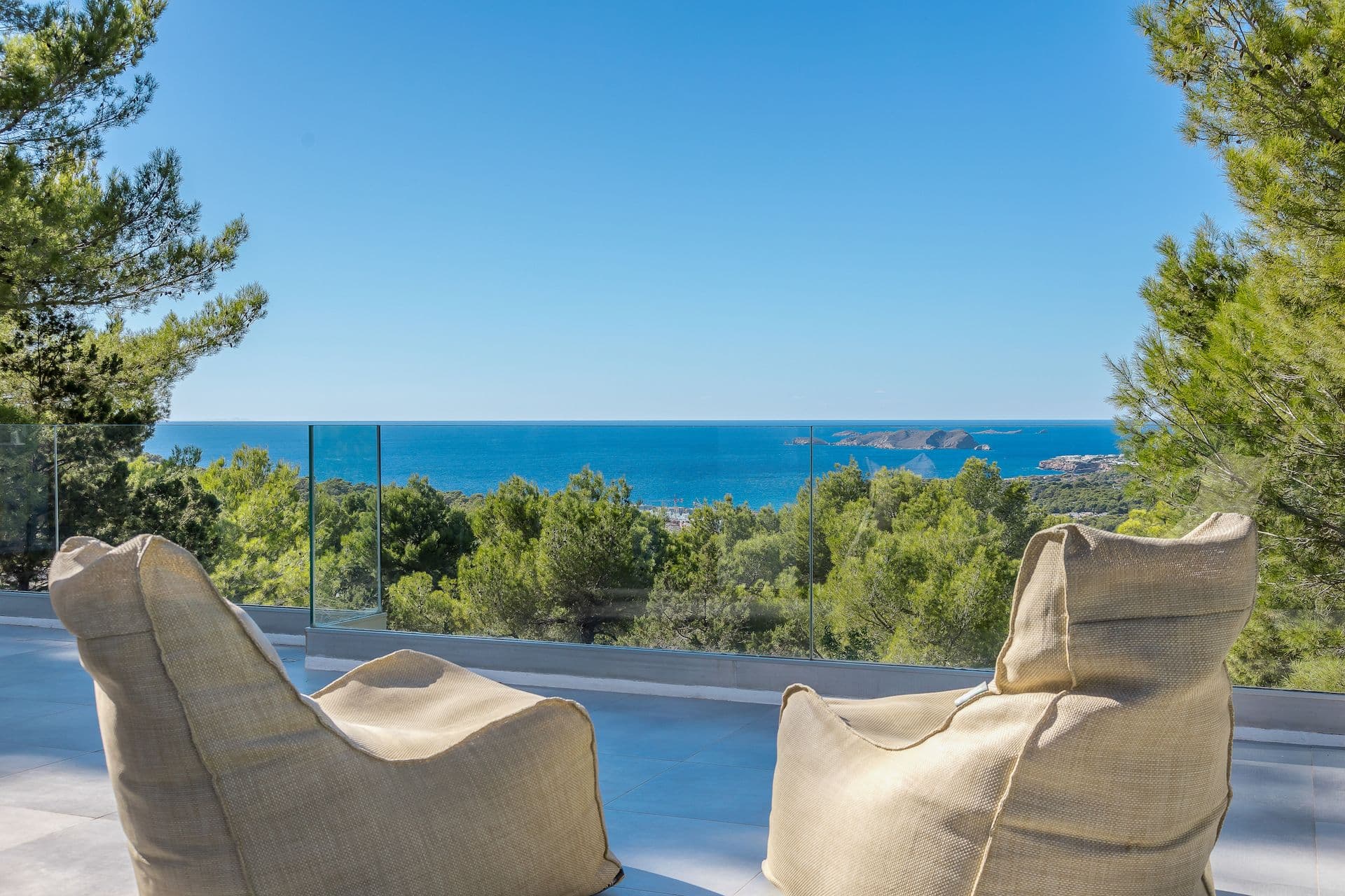 Sea view from the terrace framed by two woven armchairs and pine trees.