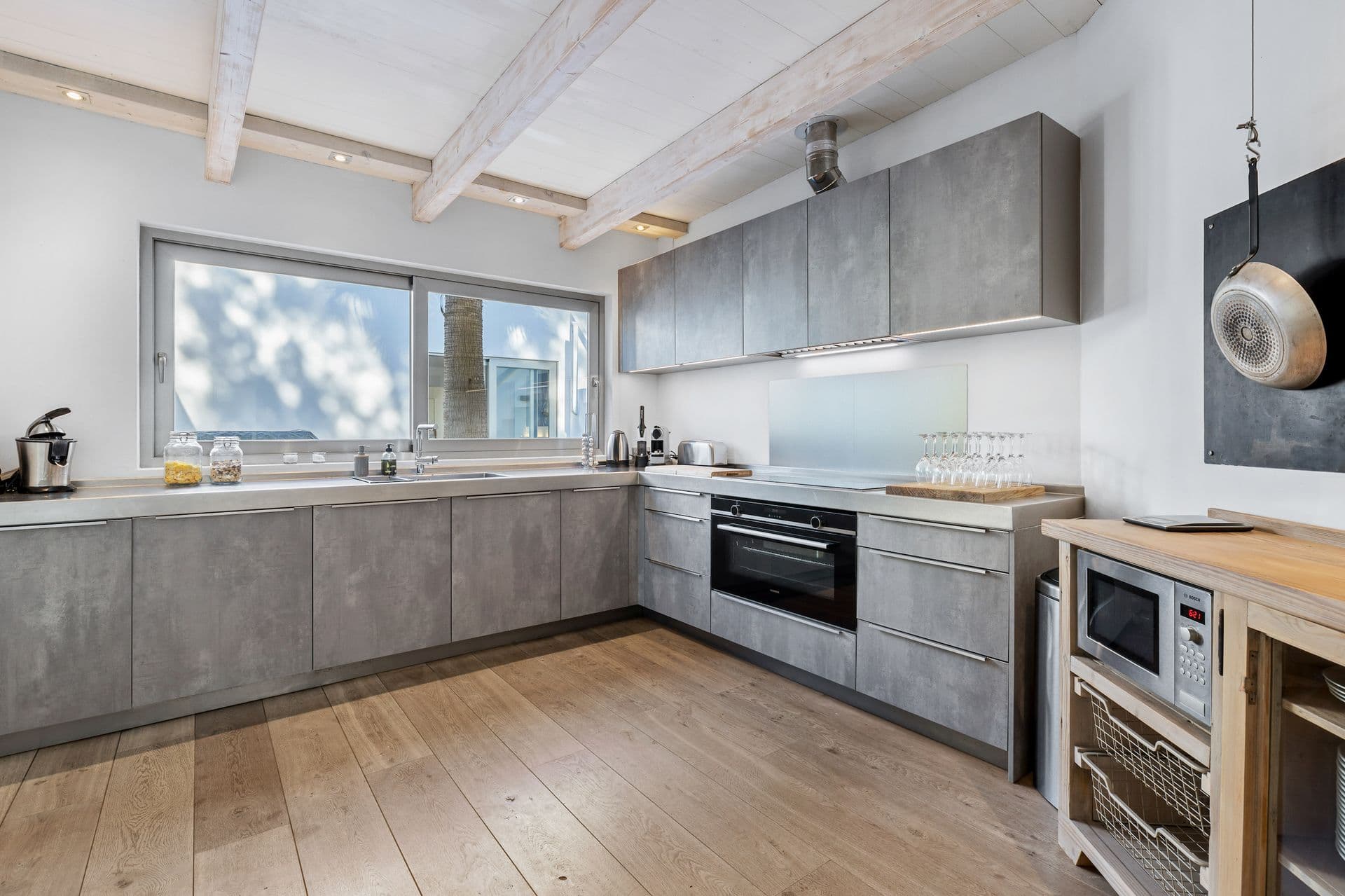 Concrete cabinetry kitchen with exposed beams and hanging pendant lights.