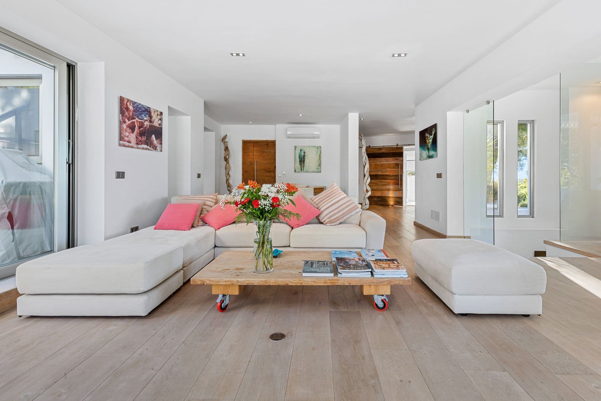 Bright living room with a white L shaped sofa, a driftwood coffee table and fresh flowers.