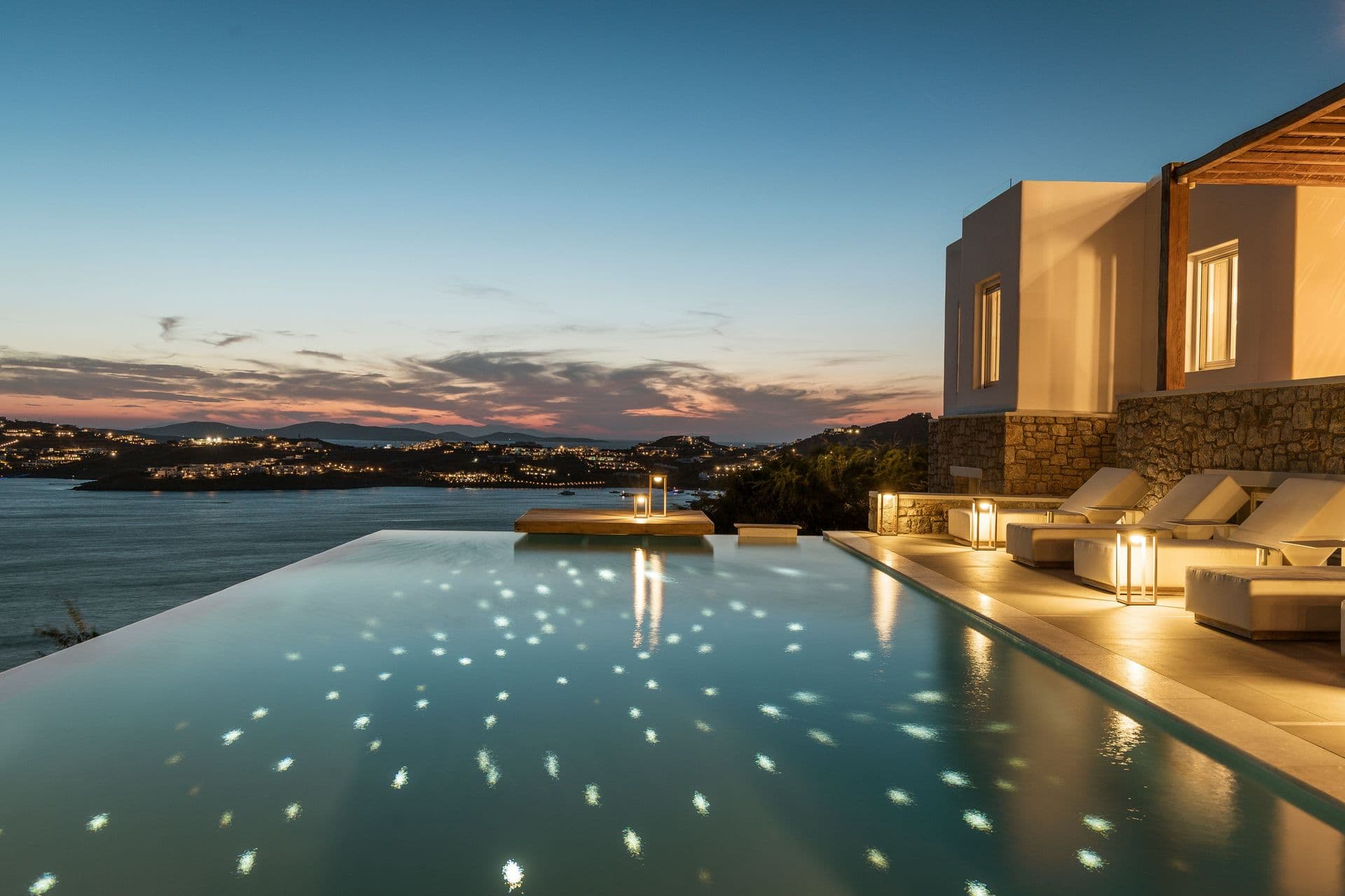 Goddess of the Clouds infinity pool lit at dusk, with sun loungers along the water's edge.