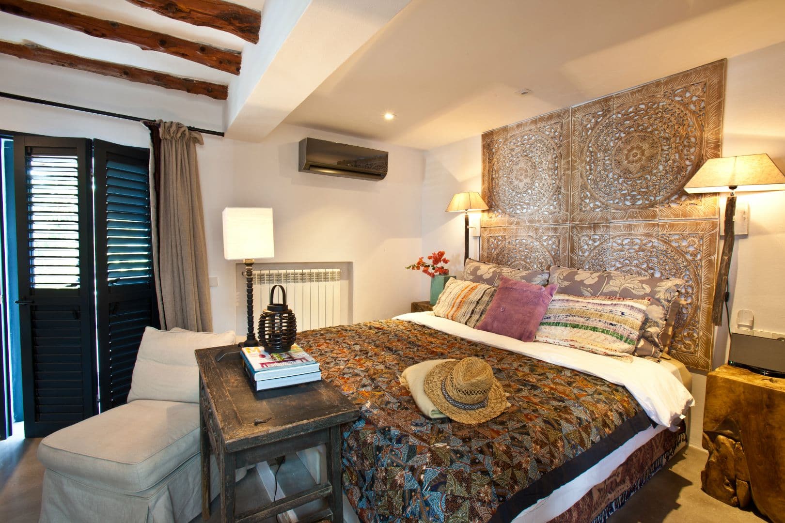 Beamed bedroom with a carved white panel headboard at Cicadas Sway, Ibiza
