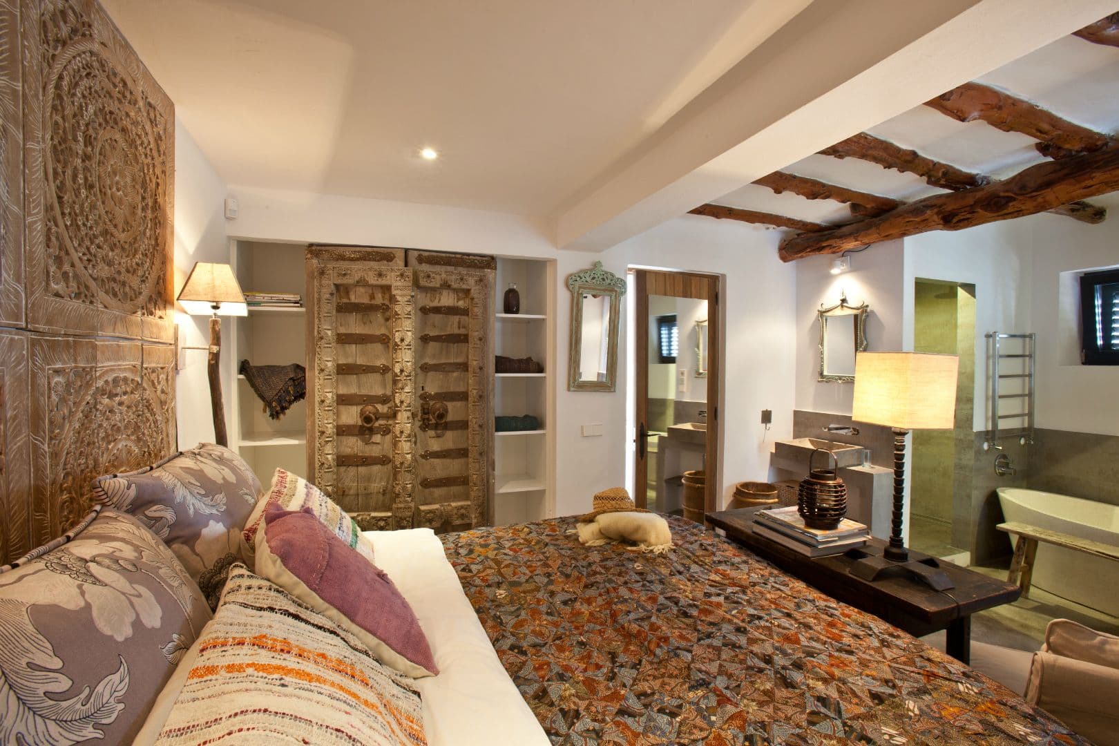 Boho bedroom suite with a carved panel headboard and beamed ceiling at Cicadas Sway, Ibiza