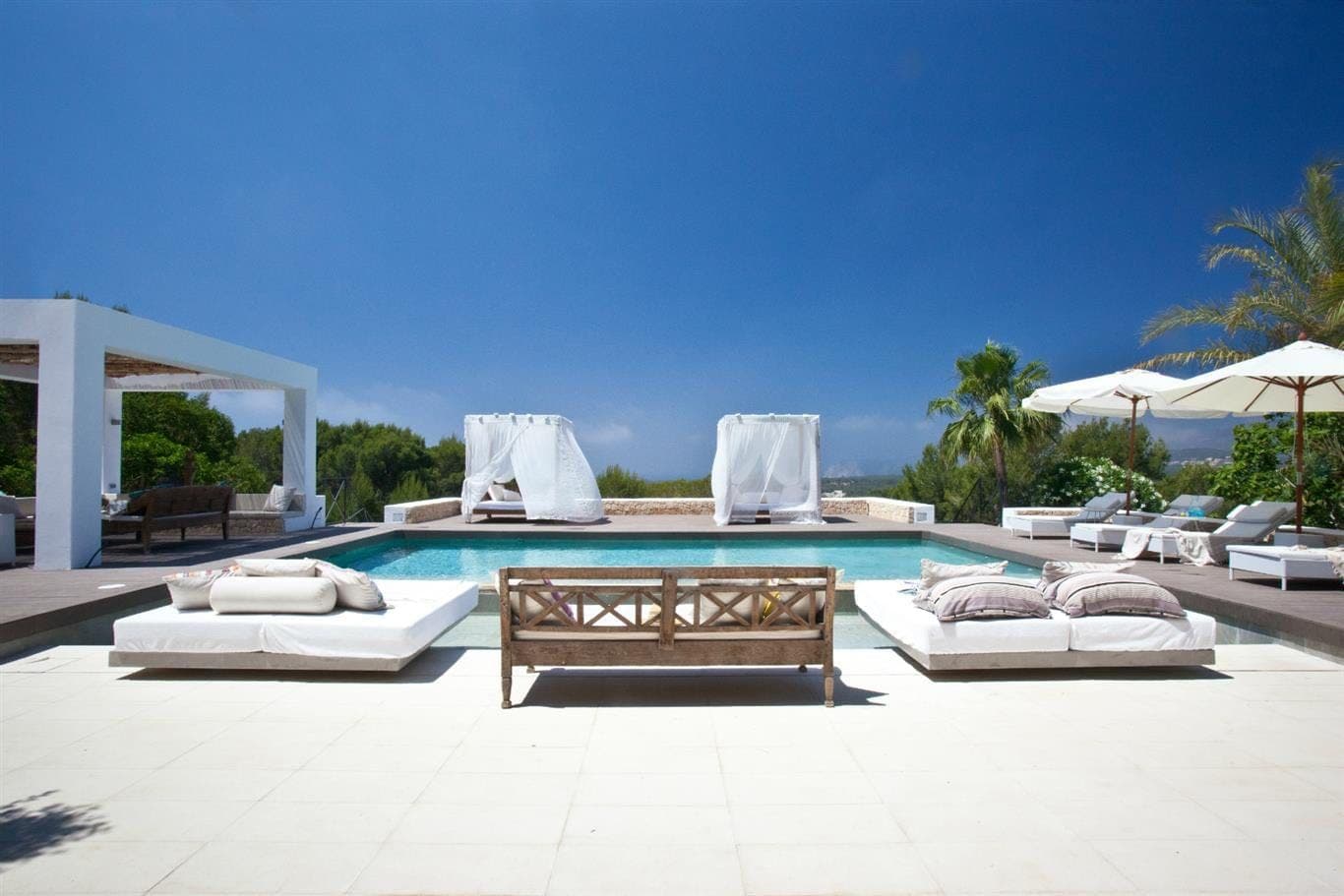 Swimming pool with white day beds, a pergola and palms at Cicadas Sway, Ibiza