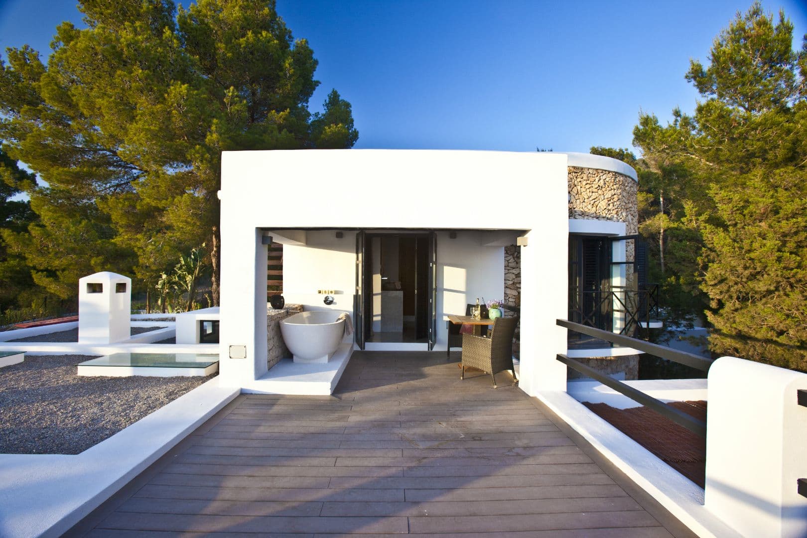 White villa with folding glass doors opening to the pool terrace among pines at Cicadas Sway, Ibiza