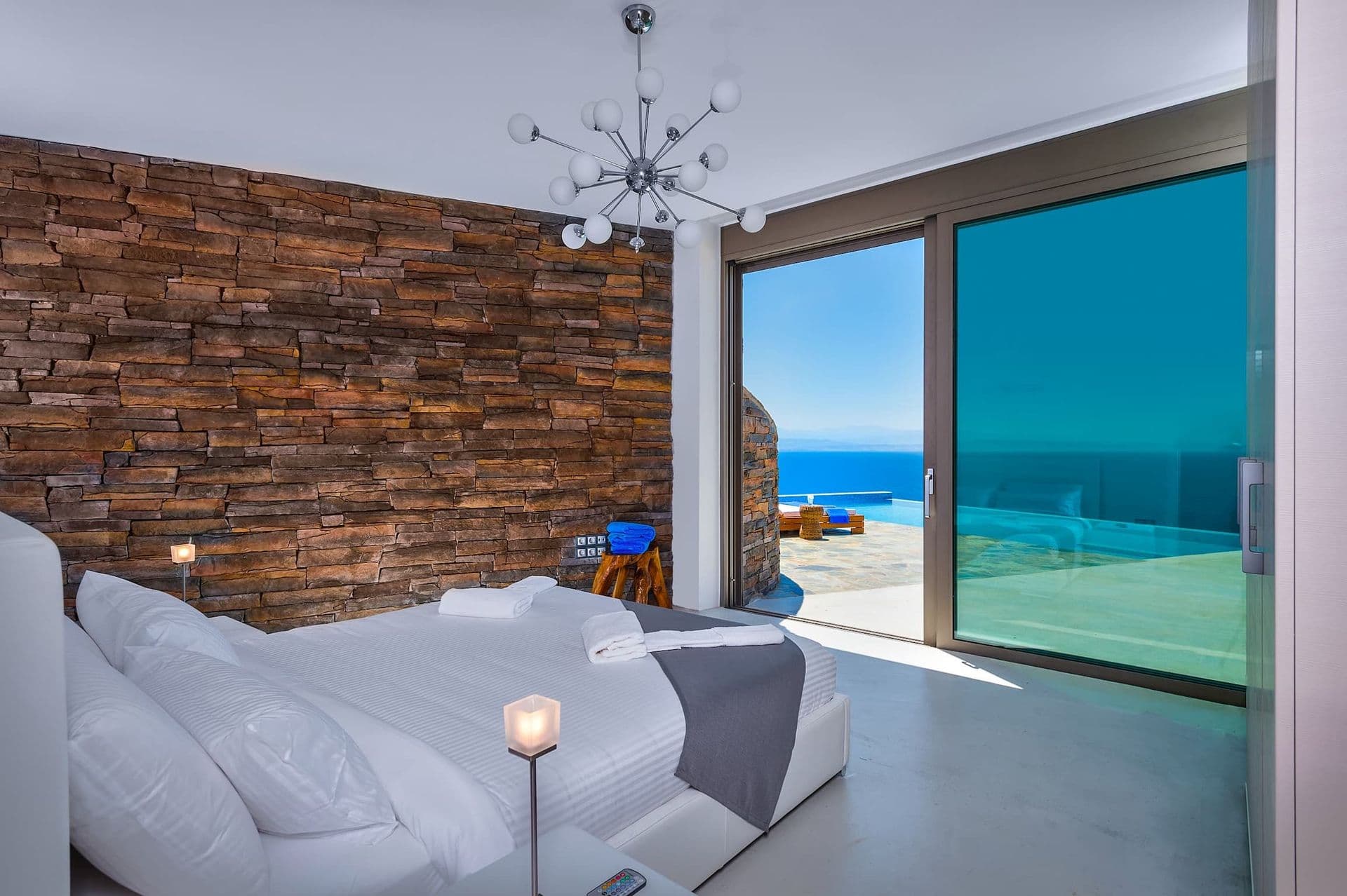 Guest bedroom with a stacked-stone wall and sliding doors onto a sea-view terrace.