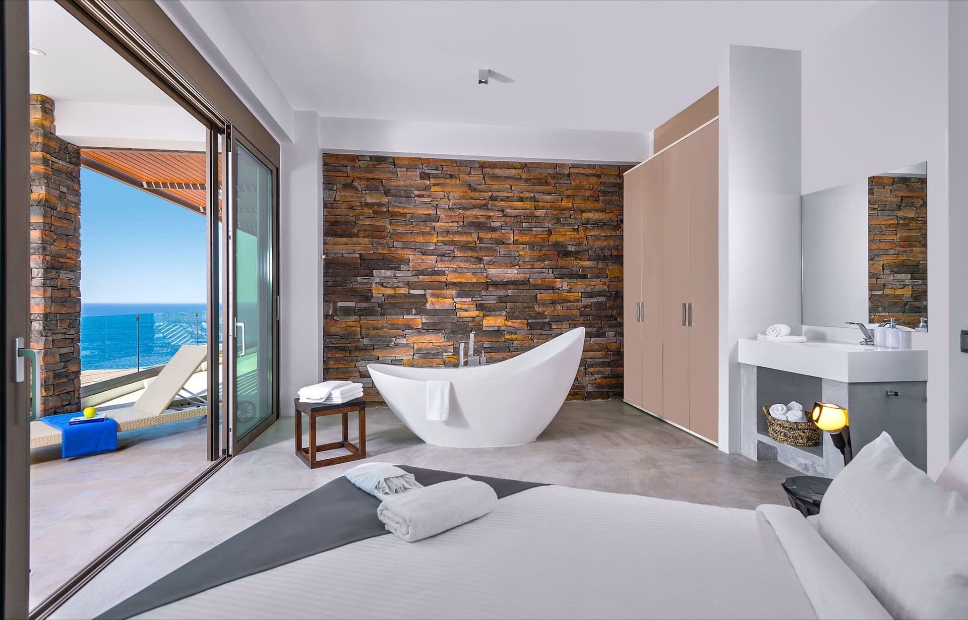 Master bedroom with a stone feature wall and floor-to-ceiling sea-facing windows.