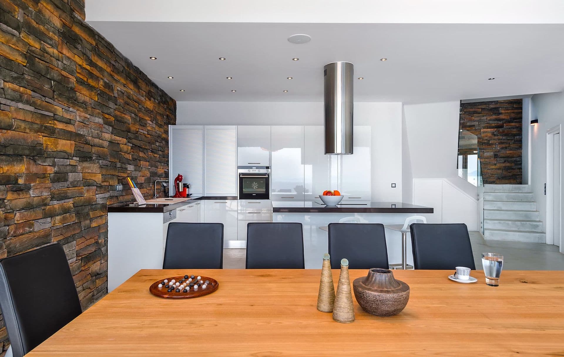 Modern white kitchen with a natural stone feature wall and dining table.