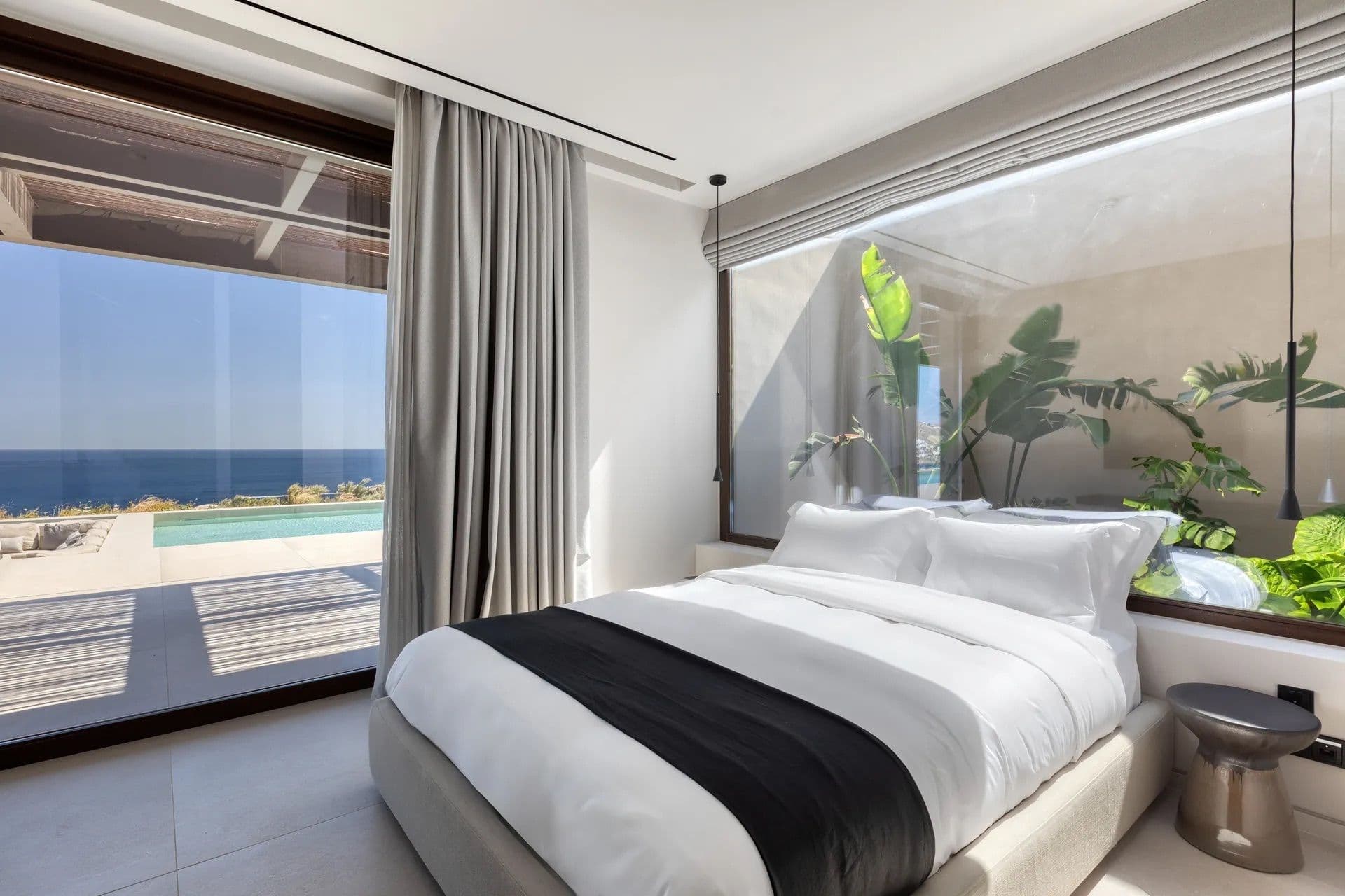 Bedroom with a black and white bed frame facing a wall of glass onto the sea view