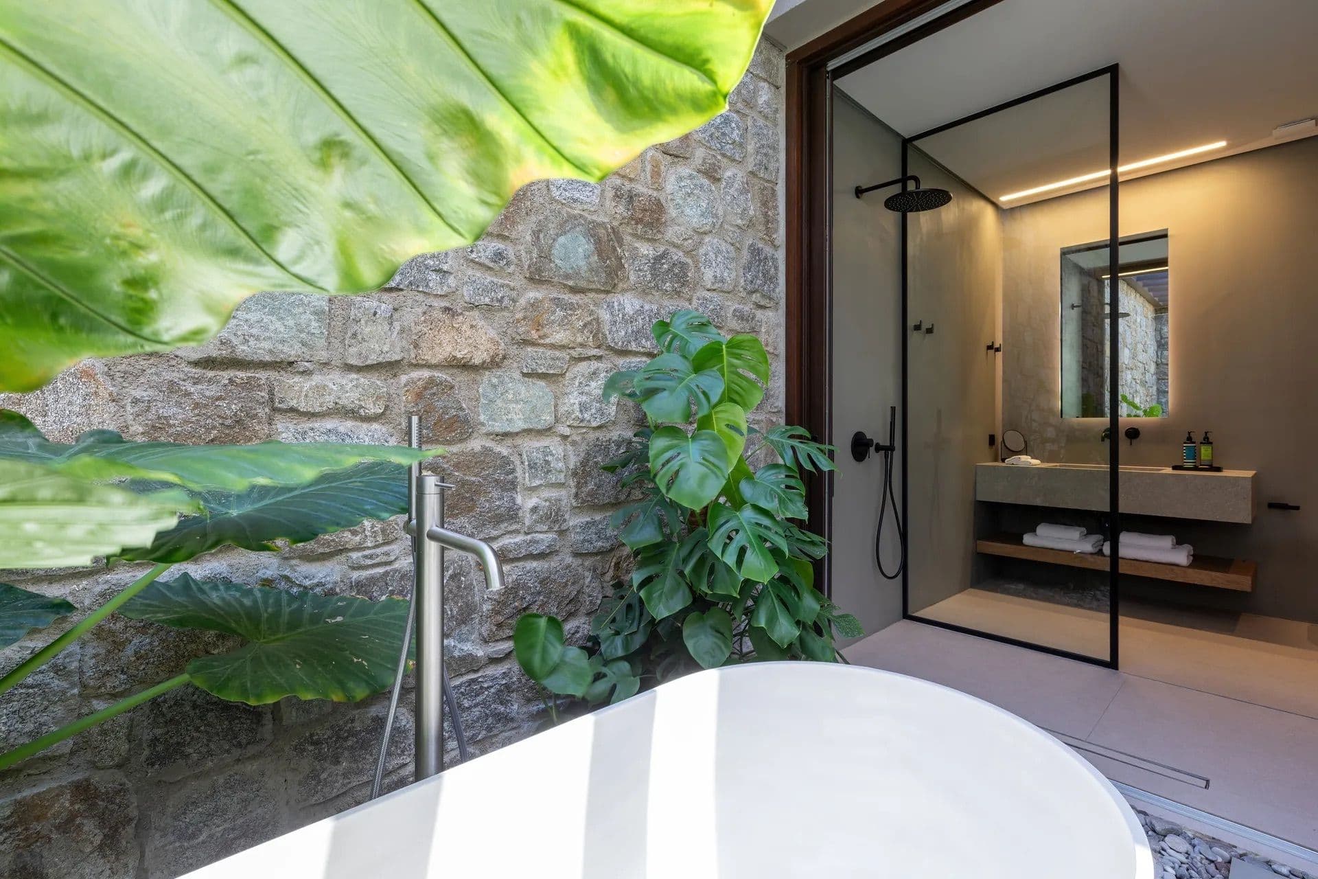 Freestanding bathtub set in a private outdoor courtyard with stone walls and greenery