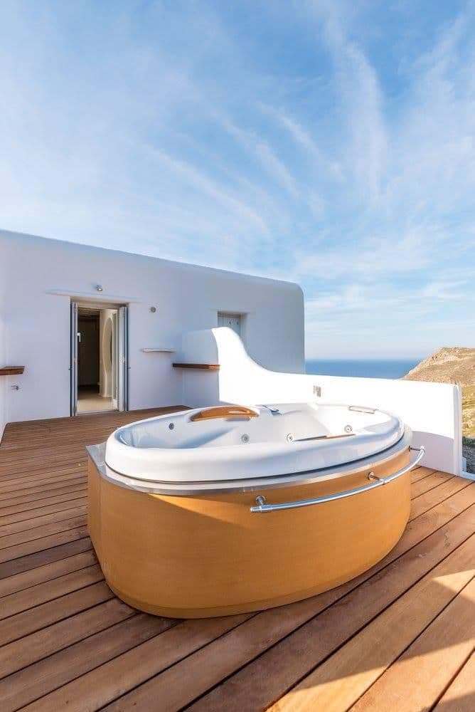 Rooftop wooden deck with a round hot tub beneath a clear blue sky