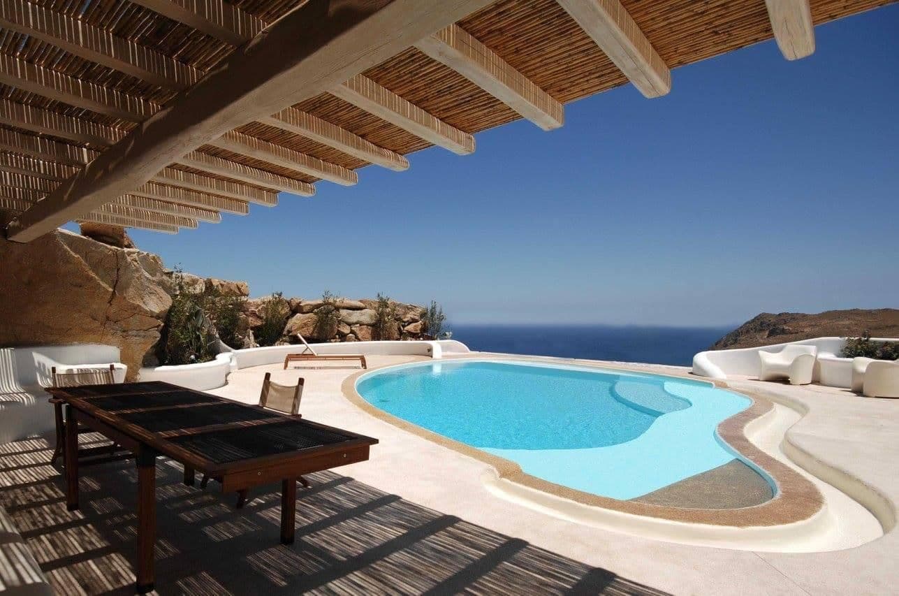 Pool with sun loungers seen beneath a reed-covered pergola