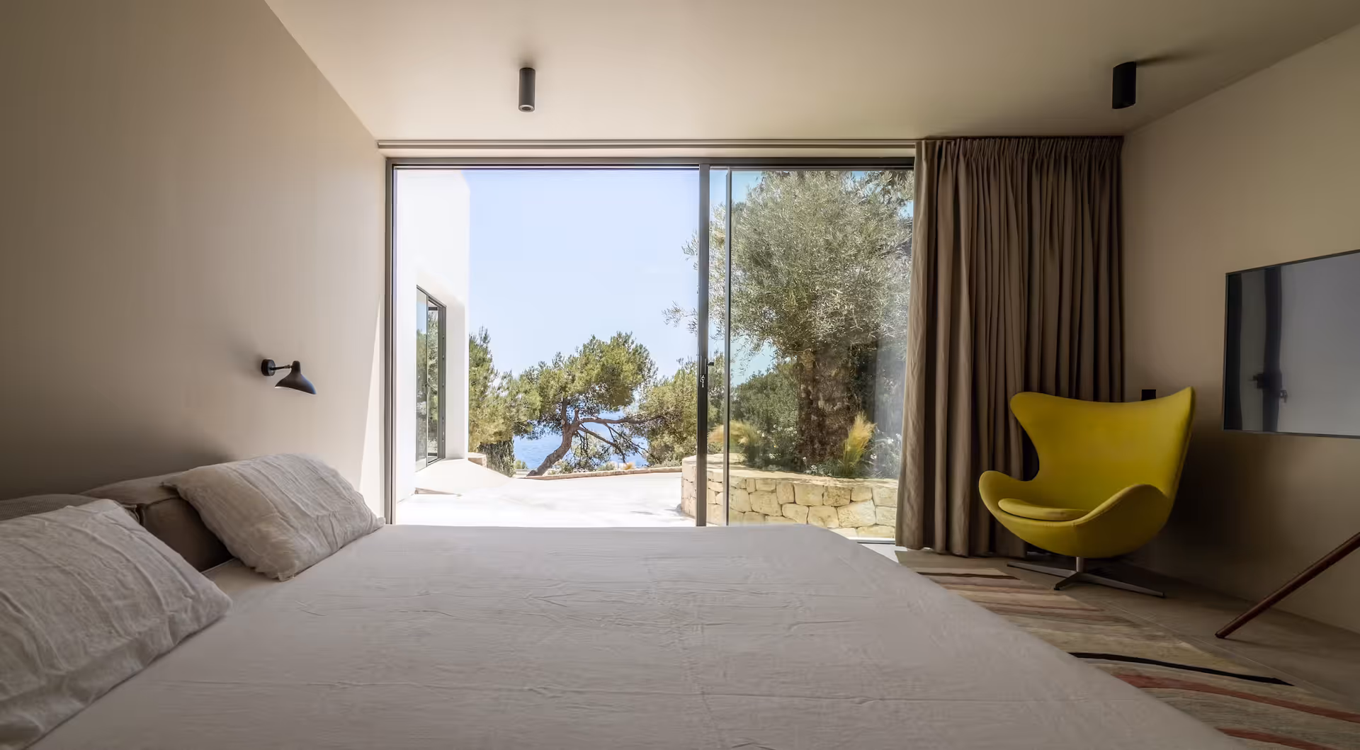 Bedroom with a mustard accent chair and glass doors opening onto a private terrace