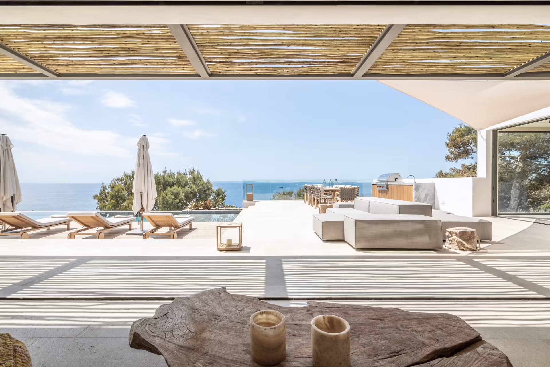 Shaded terrace lounge with low sofas and a driftwood coffee table overlooking the sea