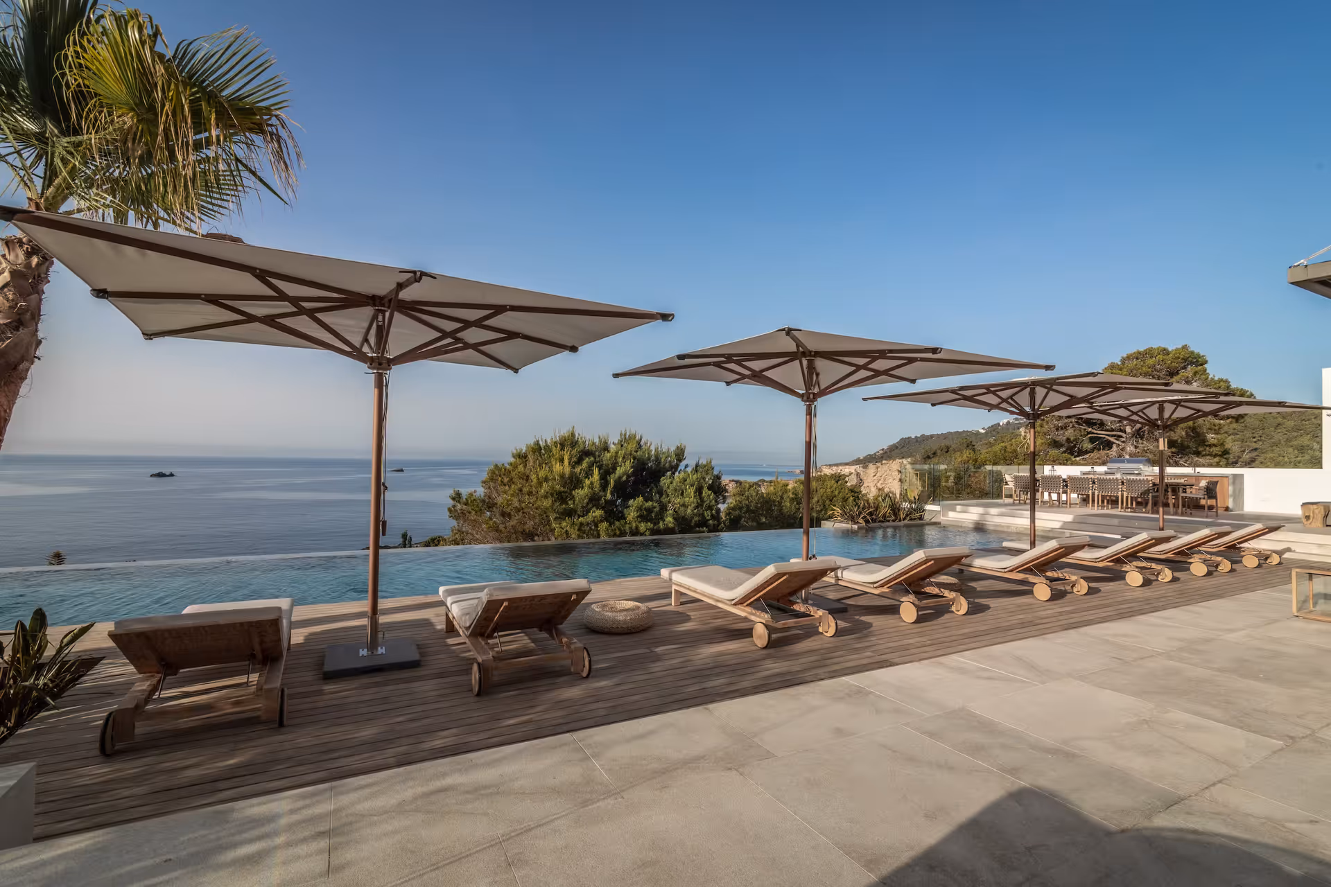 Row of sun loungers under umbrellas beside the pool overlooking the sea