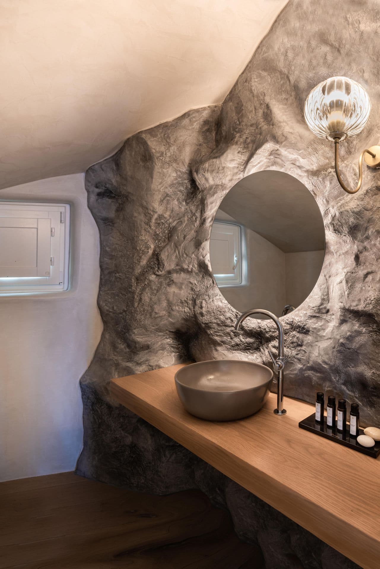 Cave-style bathroom vanity carved into volcanic rock with a round mirror