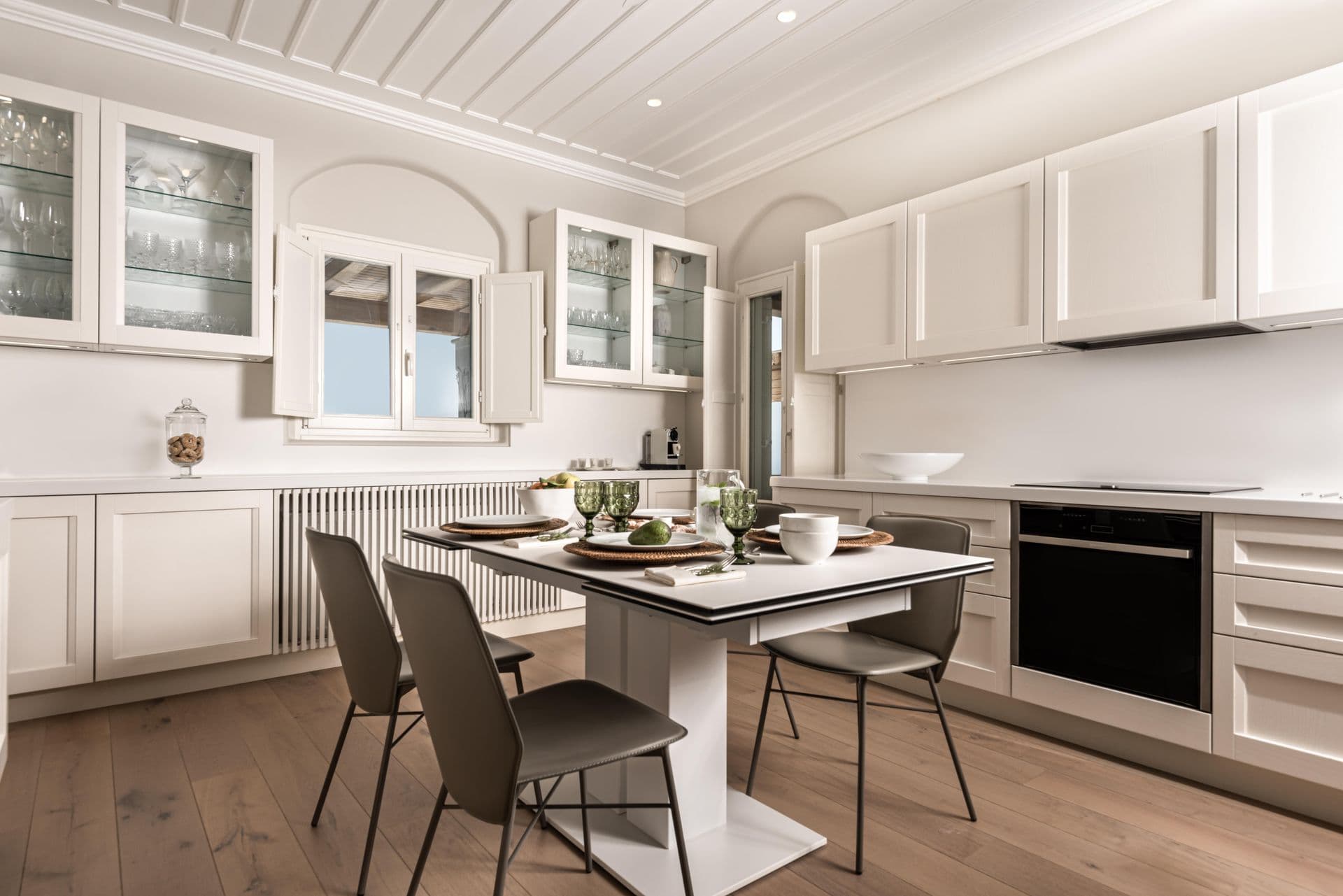 White kitchen with glass-fronted cabinetry and a small dining table