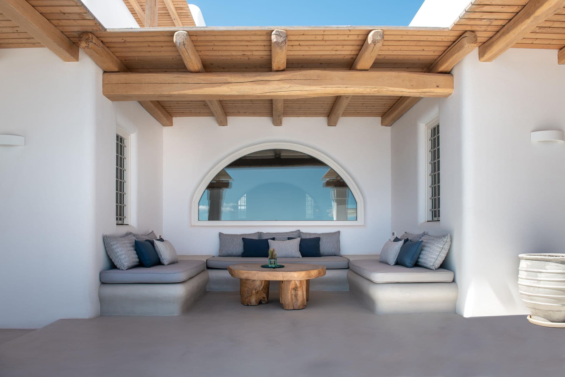 Arched outdoor lounge with blue-cushioned sofas beneath a wooden pergola