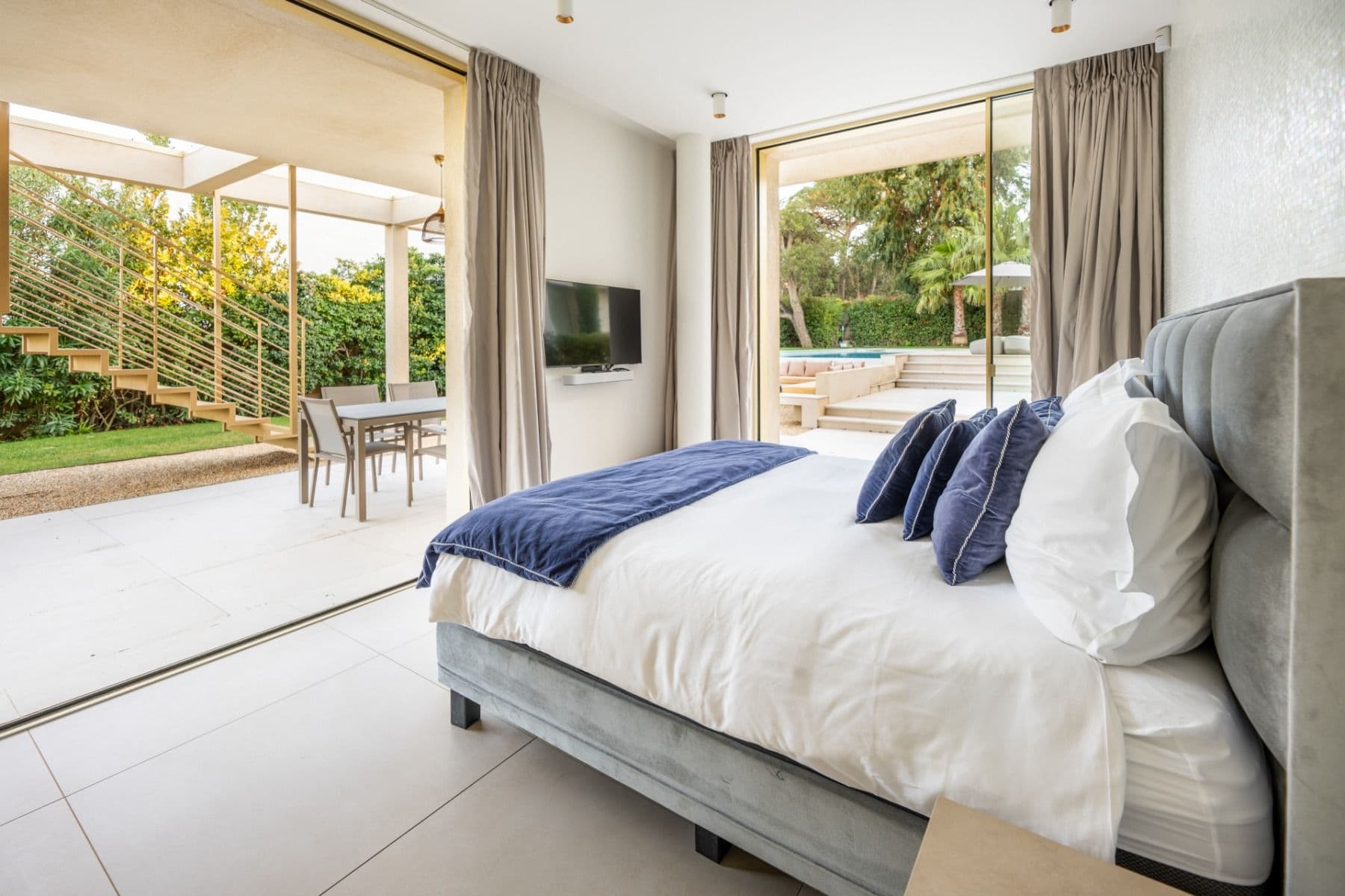 Bedroom with grey upholstered bed and sliding doors opening onto the garden