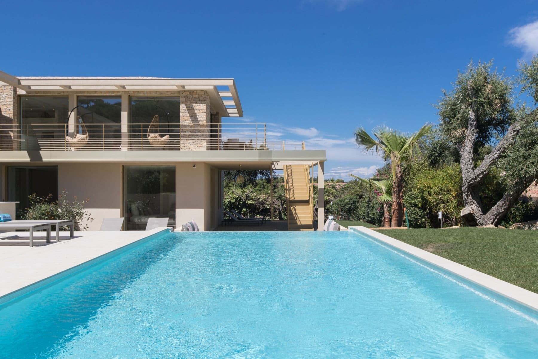 Contemporary two-storey villa with a long swimming pool and manicured lawn under blue sky