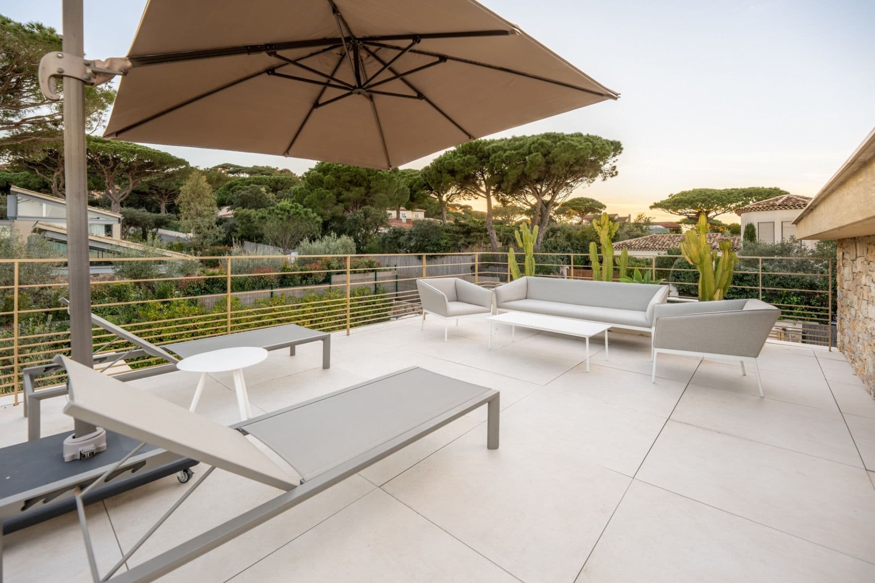 Terrace with sun loungers and umbrella overlooking pine trees and coastline