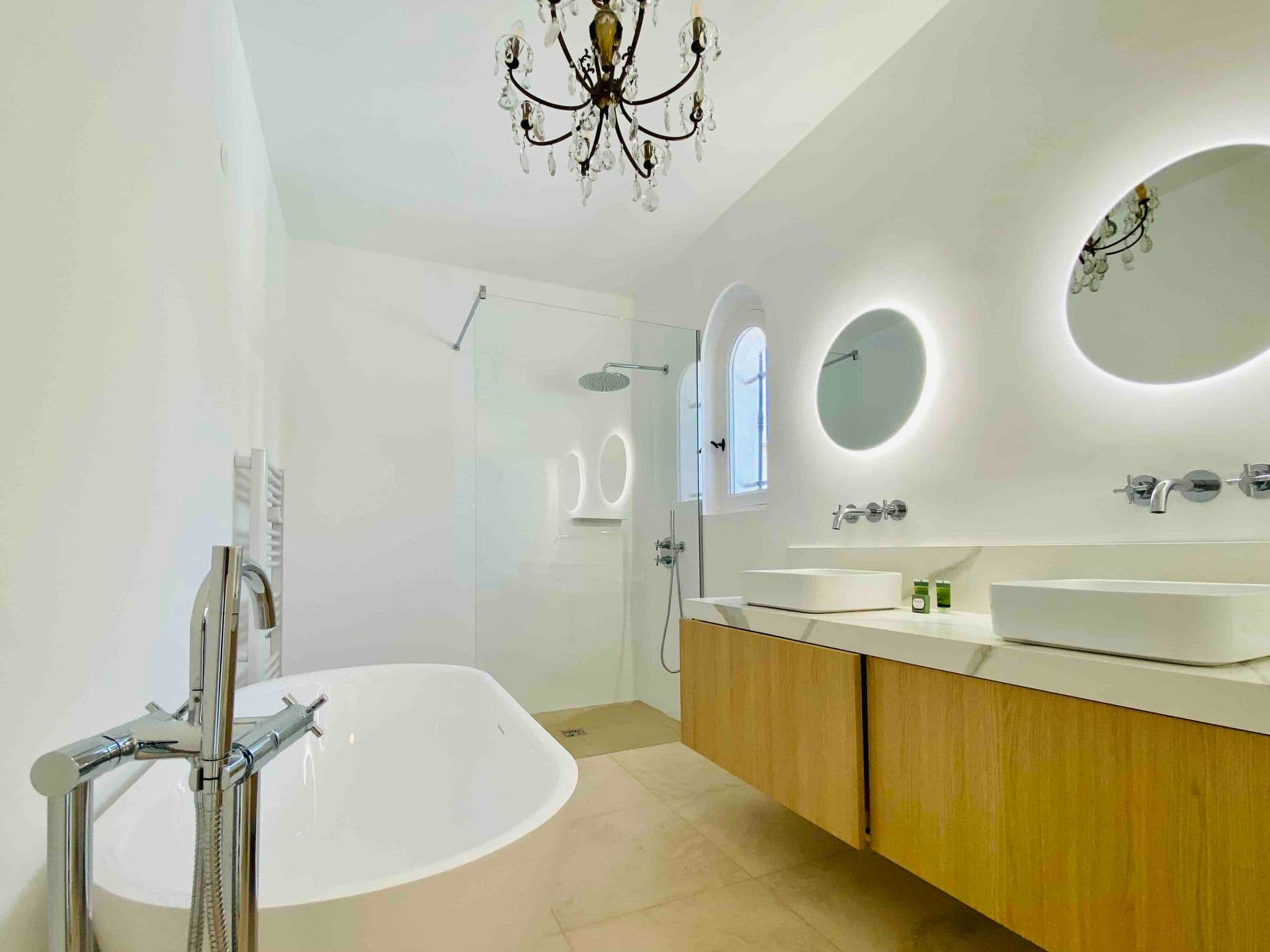 White bathroom with double vanity, round mirrors and freestanding tub