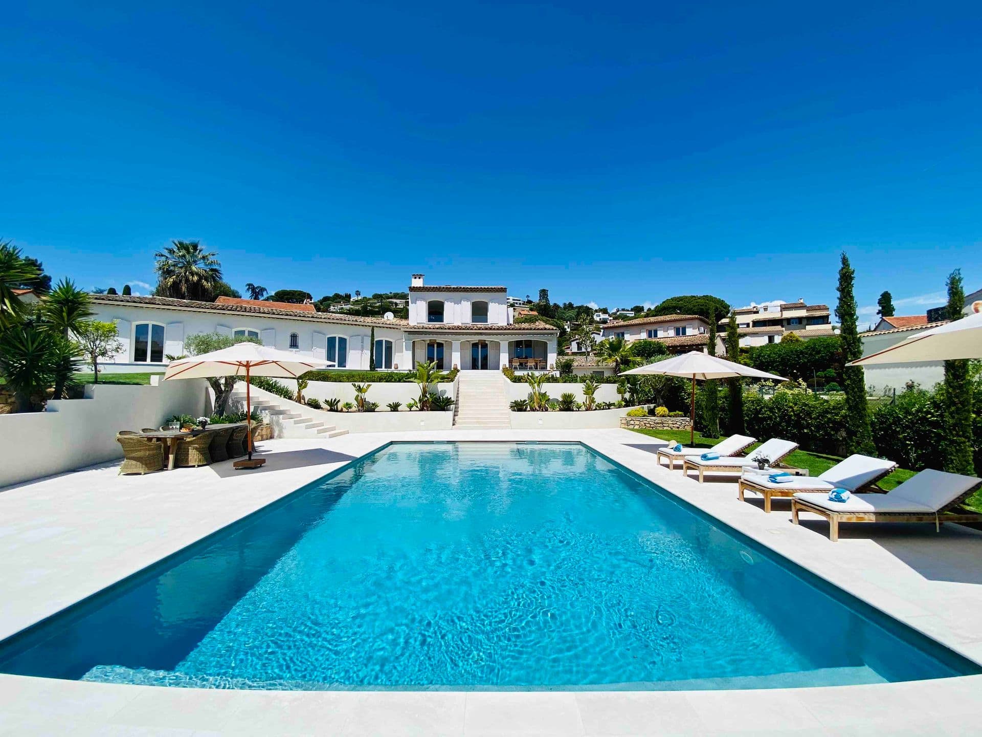 Long swimming pool with sun loungers and umbrellas beside a white villa