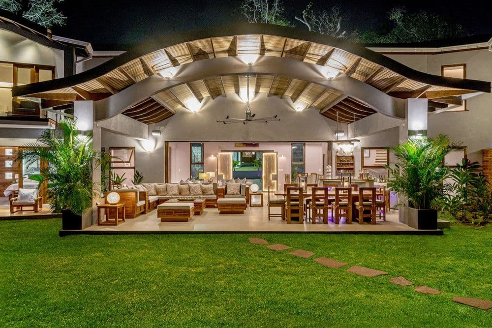 Open living pavilion with a curved timber roof lit at night at Promiseas