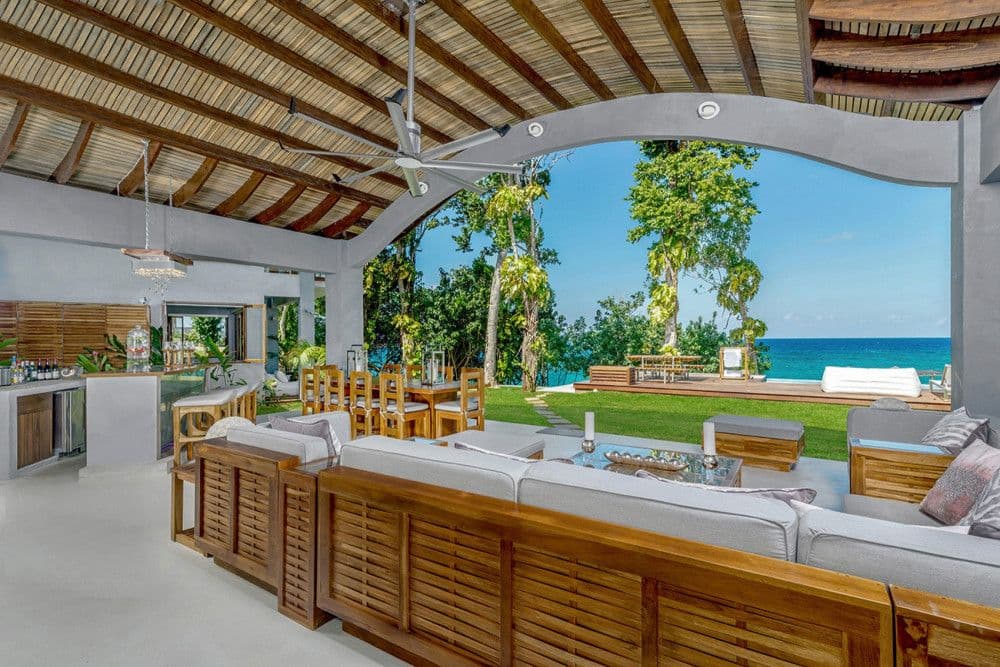 Covered outdoor lounge and bar opening to the lawn and sea at Promiseas