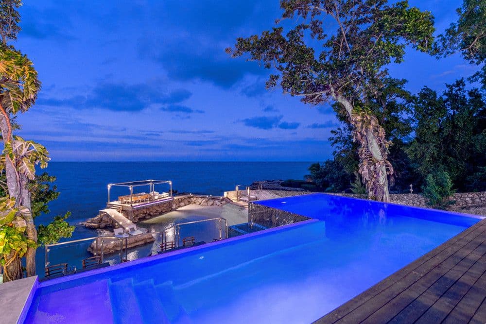 Infinity pool lit at dusk above the cove and gazebo at Promiseas