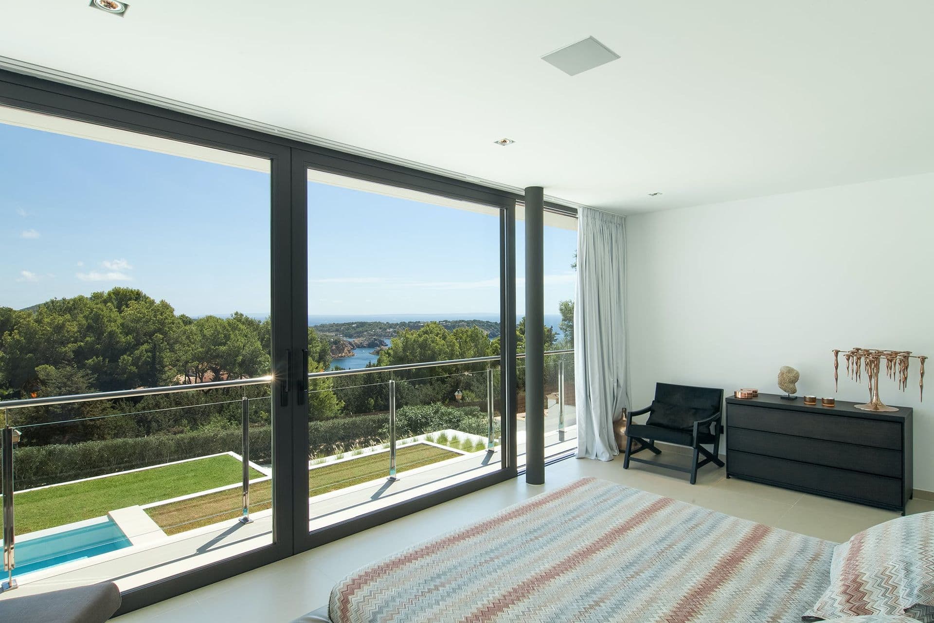 Bedroom with full-height glass doors opening to a balcony with pool and countryside views