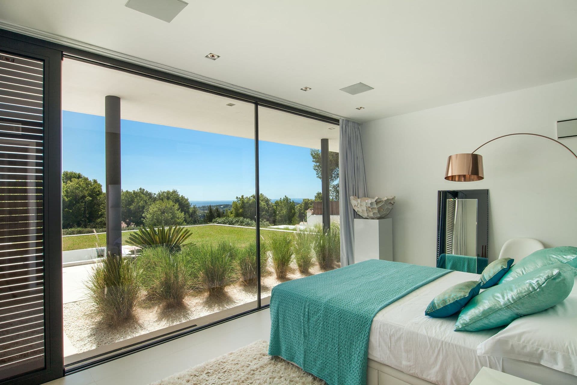 Bedroom with teal accent cushions and panoramic garden-view glazing