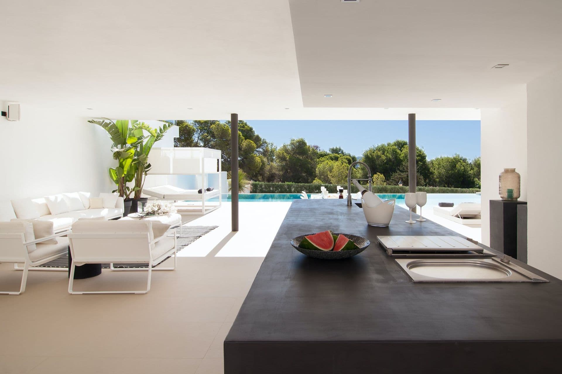 Open-plan living room with white sofas and floor-to-ceiling glass doors onto the pool terrace