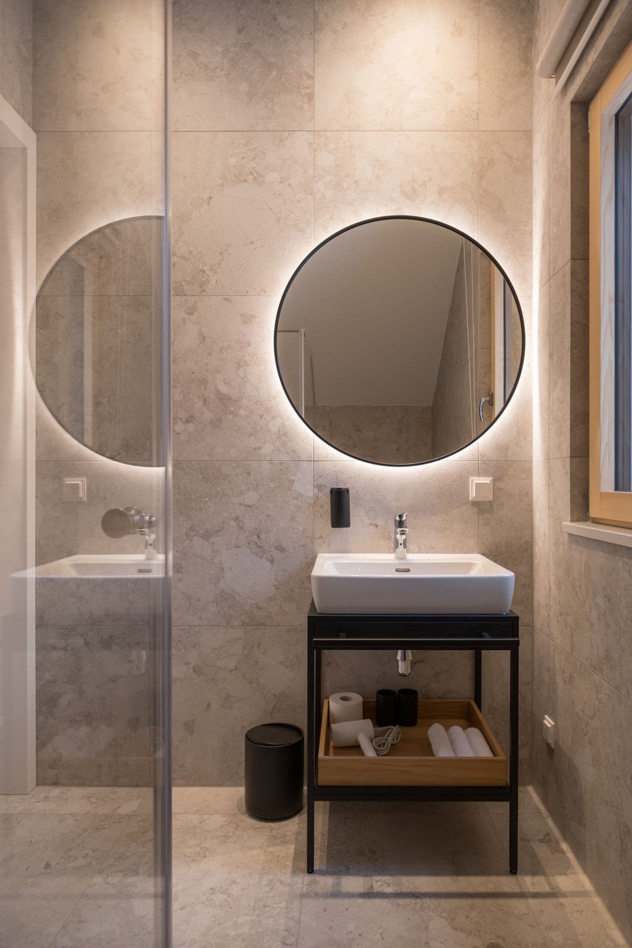 Bathroom with round mirror, stone-topped vanity and open shelving