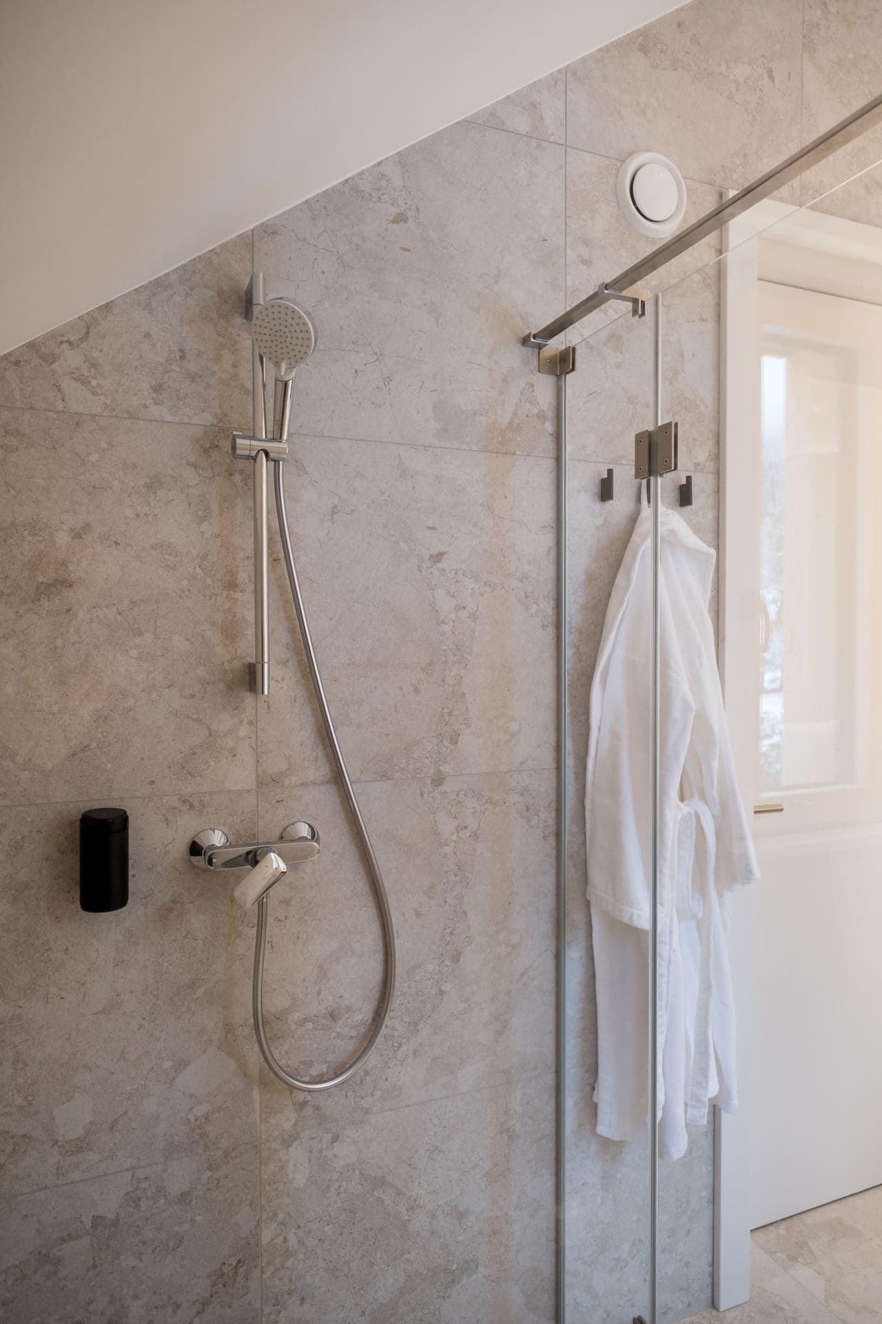 Walk-in shower with rainfall head and hanging bathrobe beside a curtained window