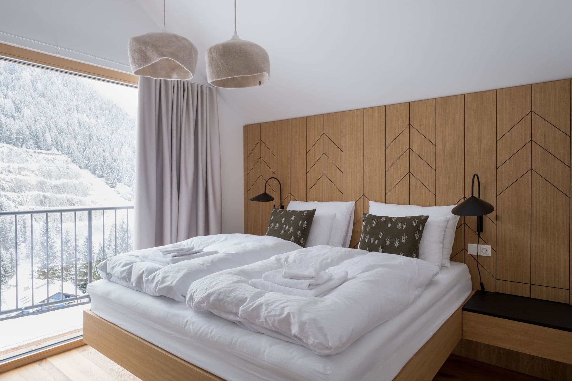 Bedroom with chevron wood panelled headboard and window onto the mountains