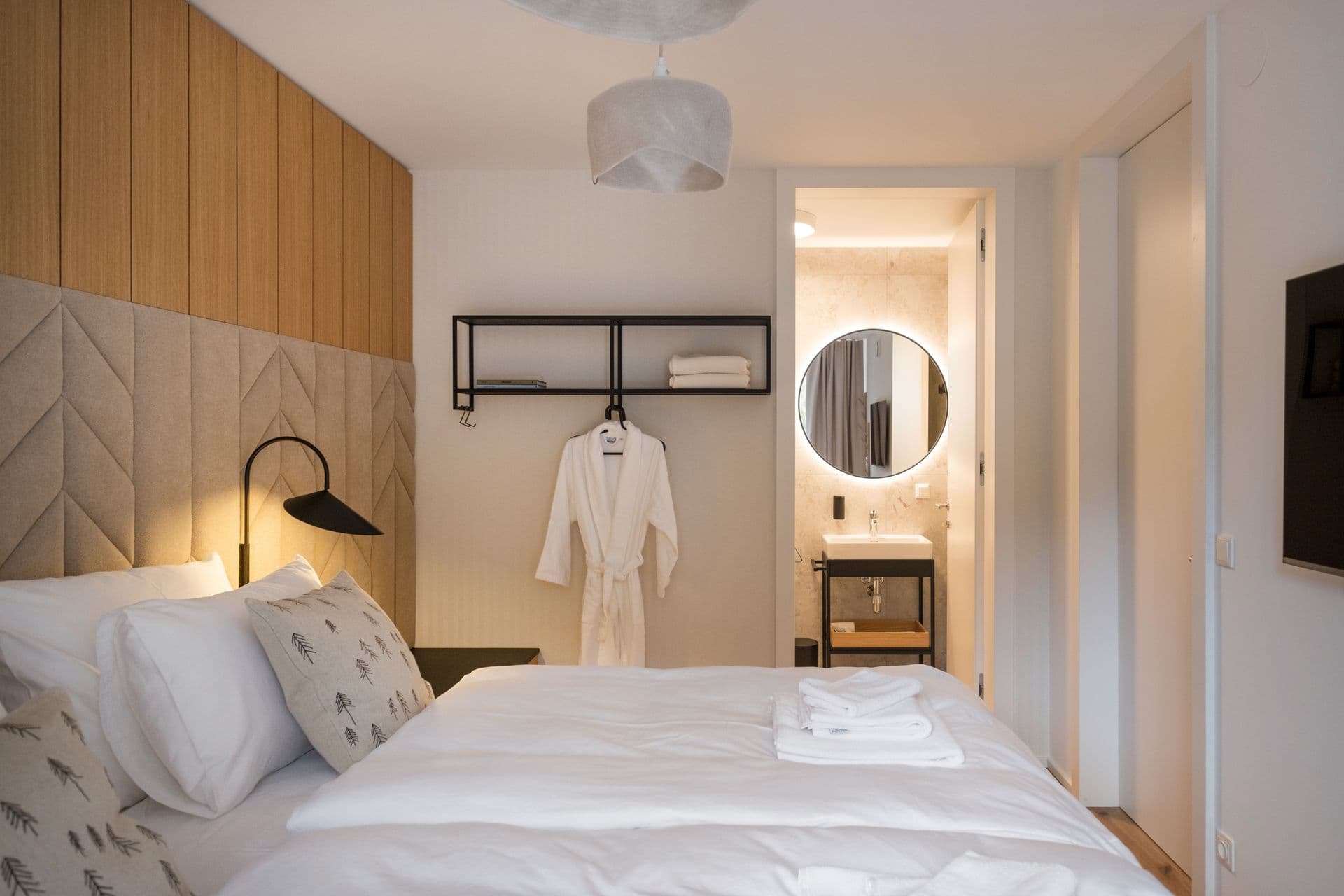 Bedroom with white bedding, hanging robe and view through to the ensuite bathroom