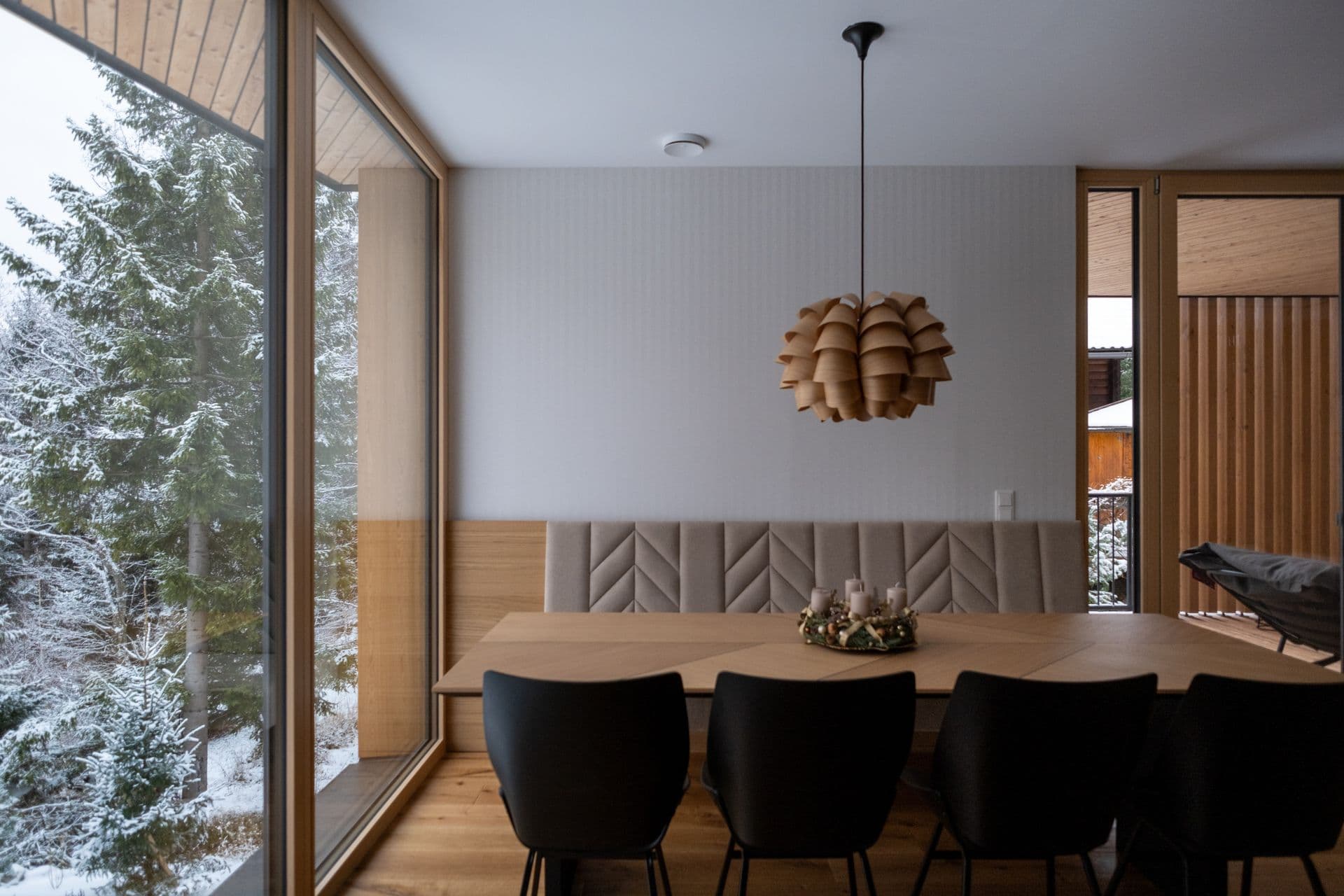 Dining table for eight beside a floor-to-ceiling window with snow-covered trees outside