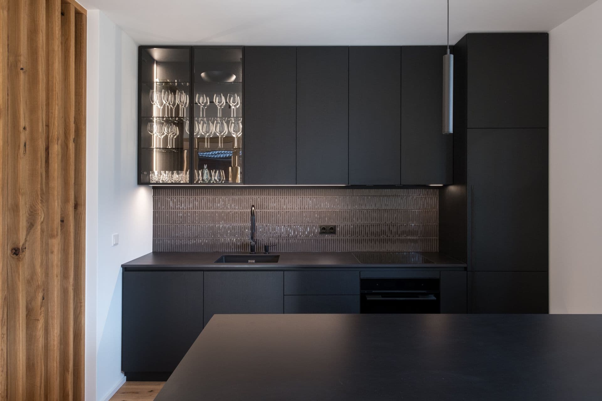 Matte black kitchen counter with glassware cabinets and tiled splashback