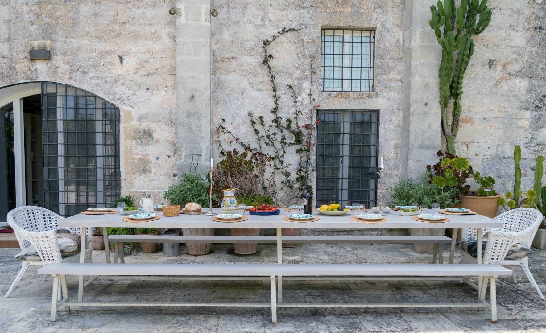 Long outdoor dining table set against the stone facade of the farmhouse