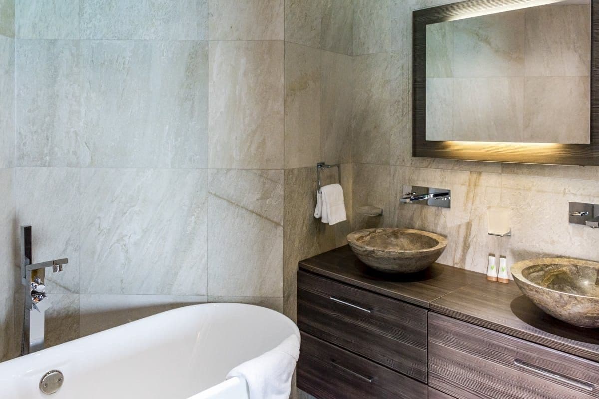 Stone en-suite bathroom with a freestanding bath and bowl basins at Sunlight Breeze, Antigua