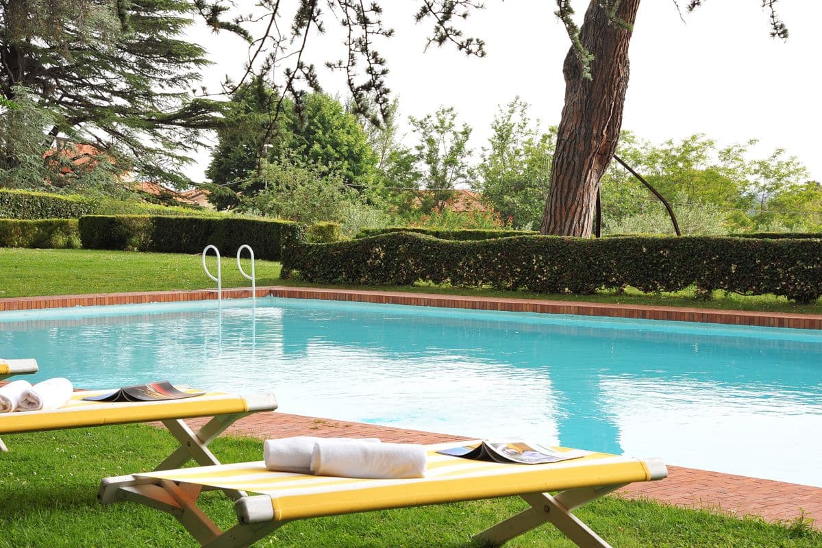 Rectangular swimming pool with yellow sun loungers set on a lawn bordered by hedges at Midnight Ball