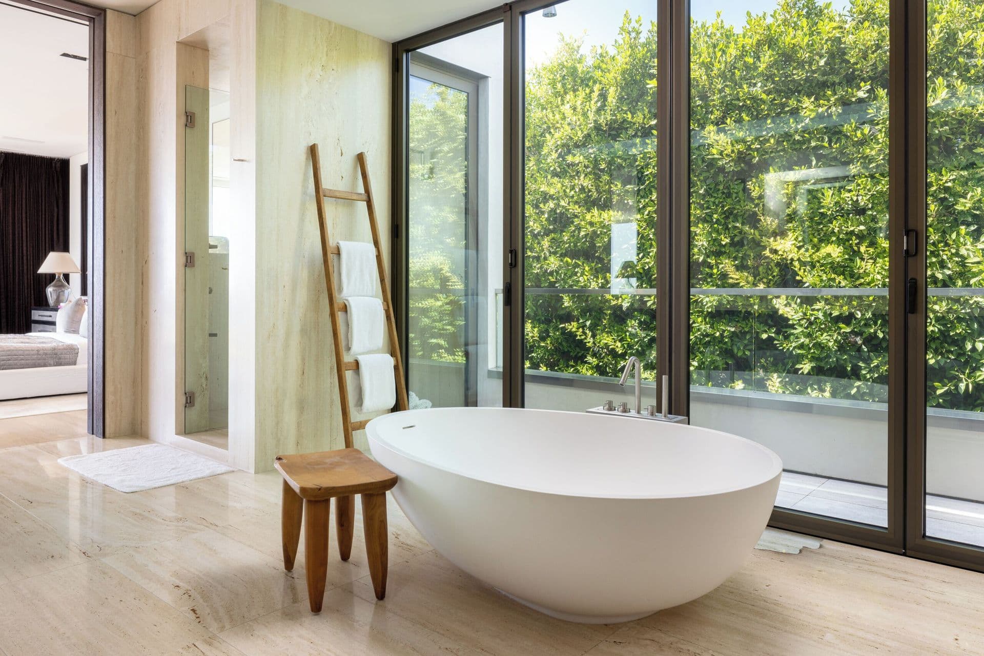 Freestanding bathtub beside a glass wall overlooking tree canopy