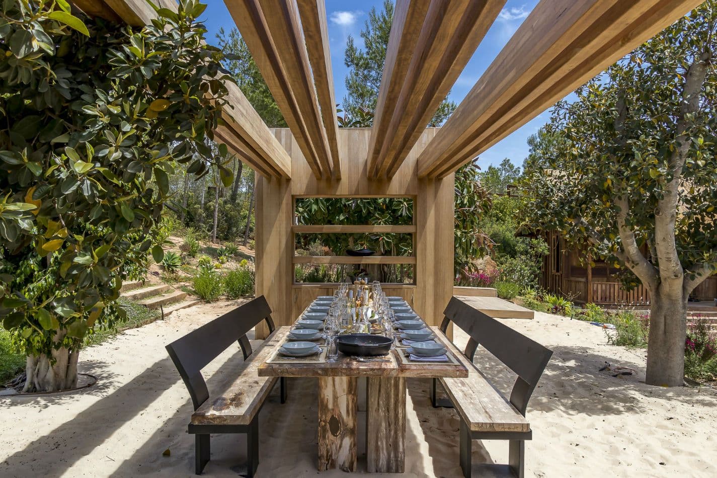 Rustic outdoor dining table under a timber pergola on sand at Aphrodite's Oasis, Ibiza