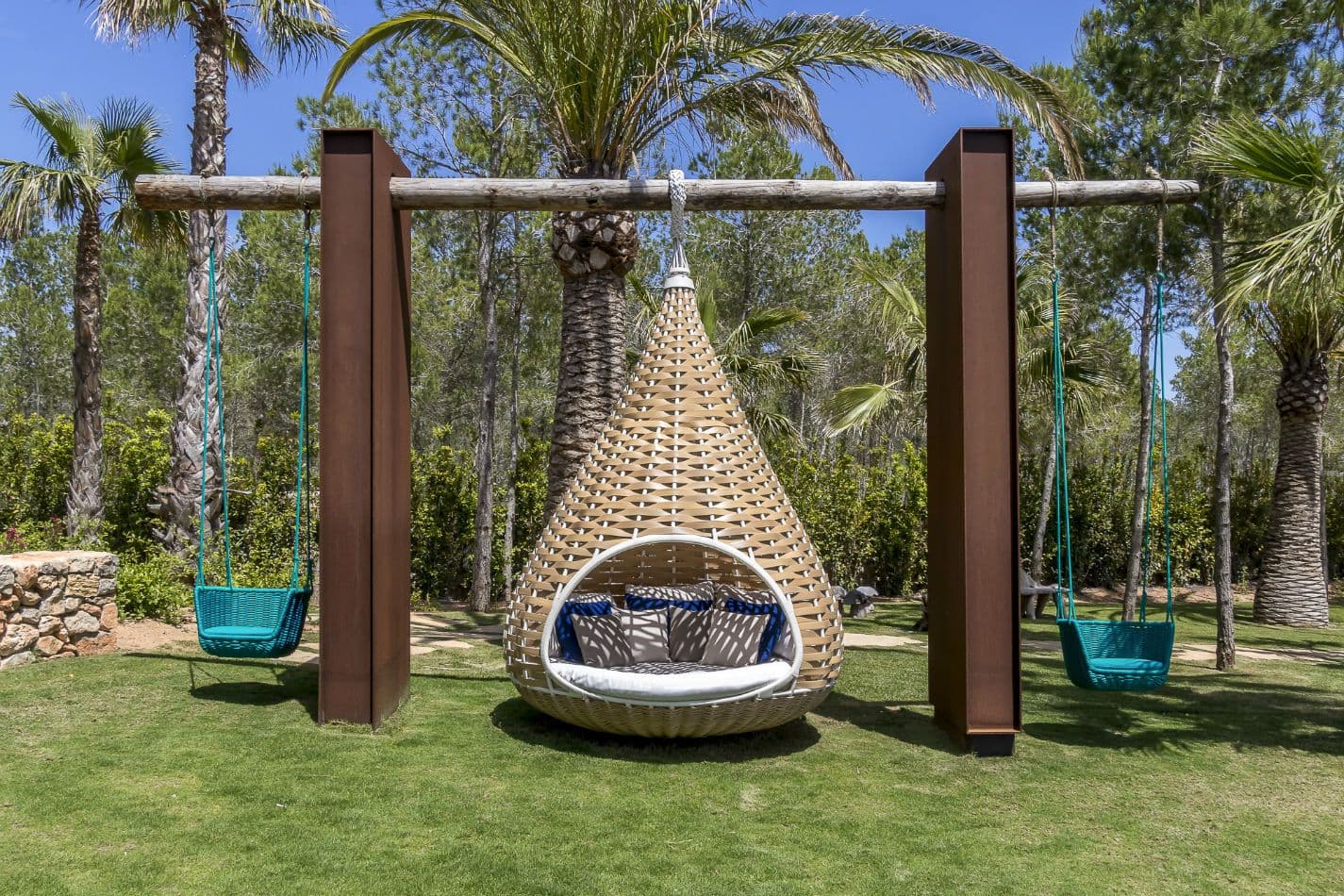 Hanging teardrop swing seats on a lawn between palms at Aphrodite's Oasis, Ibiza