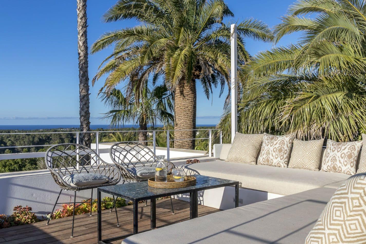 Sun terrace with rattan chairs and a day bed among palms above the sea at Aphrodite's Oasis, Ibiza